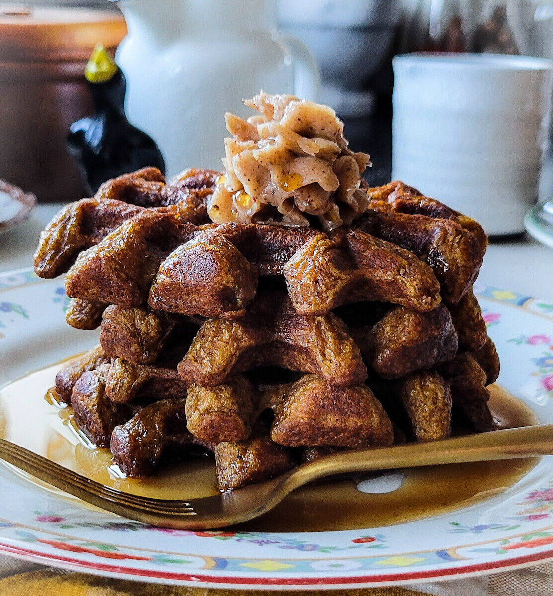 A stack of Pumpkin Waffles on a plate topped with whipped Cinnamon Honey Butter.