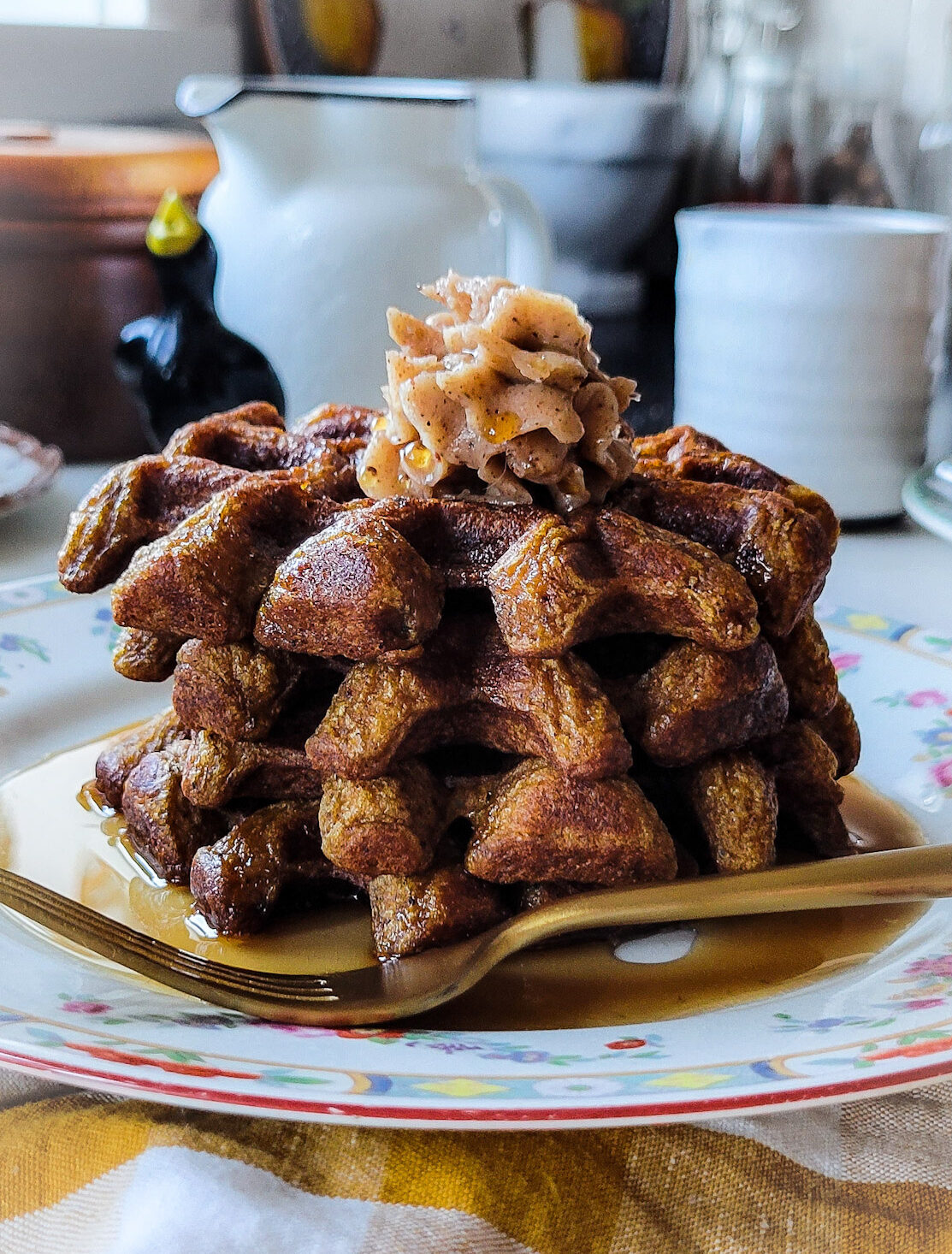 A stack of Pumpkin Waffles on a plate topped with whipped Cinnamon Honey Butter.
