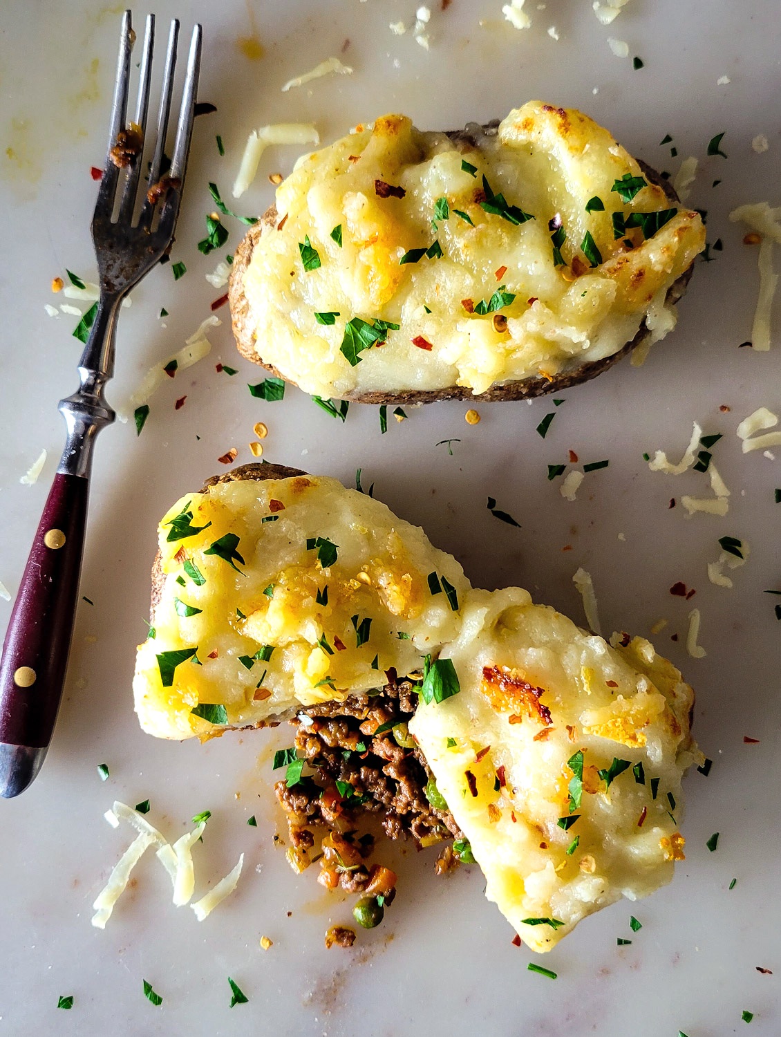Looking down on two Shepherd's Pie Stuffed Potatoes, with some of the filling spilling out from the potato.