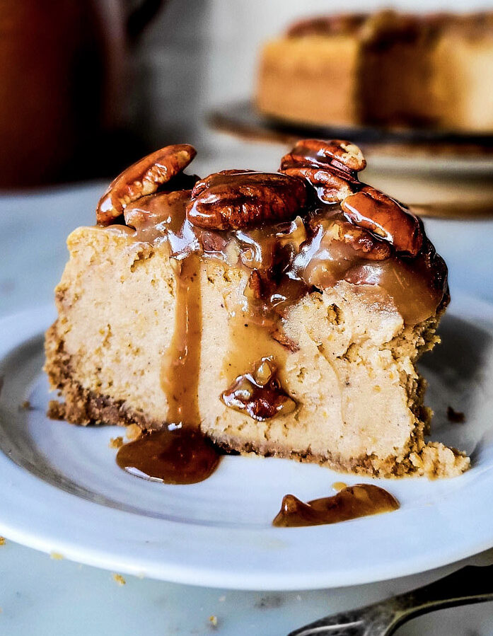 A slice of Pecan Praline Pumpkin Cheesecake with the caramel and nuts dripping down the sides.