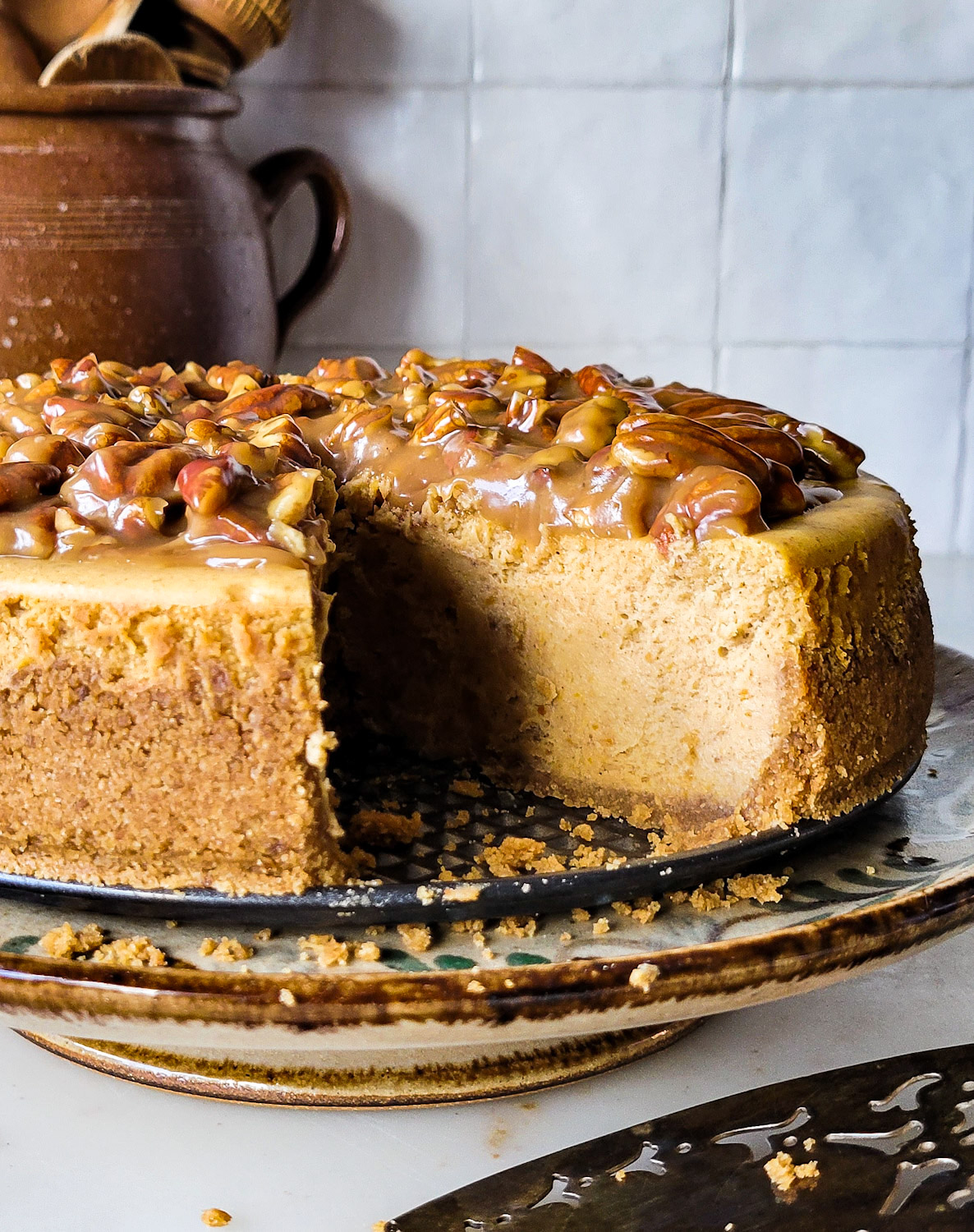 A Pecan Praline Pumpkin Cheesecake sits on a cake stand, with one slice removed.