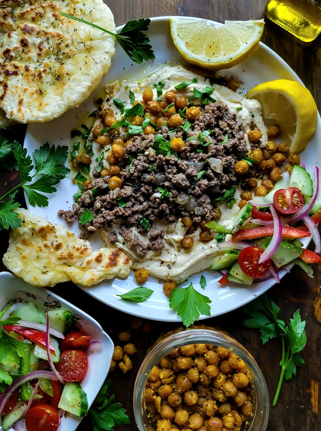 A platter filled with hummus, spiced beef and topped with Dukka Roasted Chickpeas. Flatbread and Greek salad are to the side.