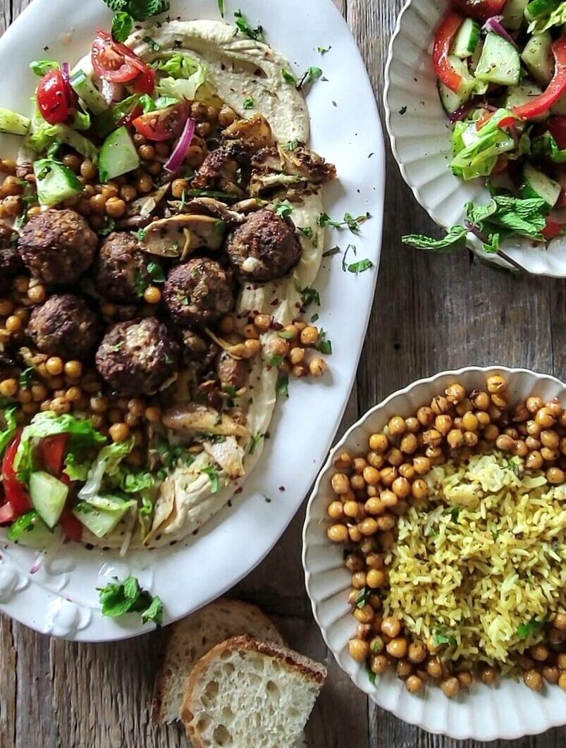 A platter with hummus, greek meatballs and dukkah roasted chickpeas has greek salad and jeera rice to the side.