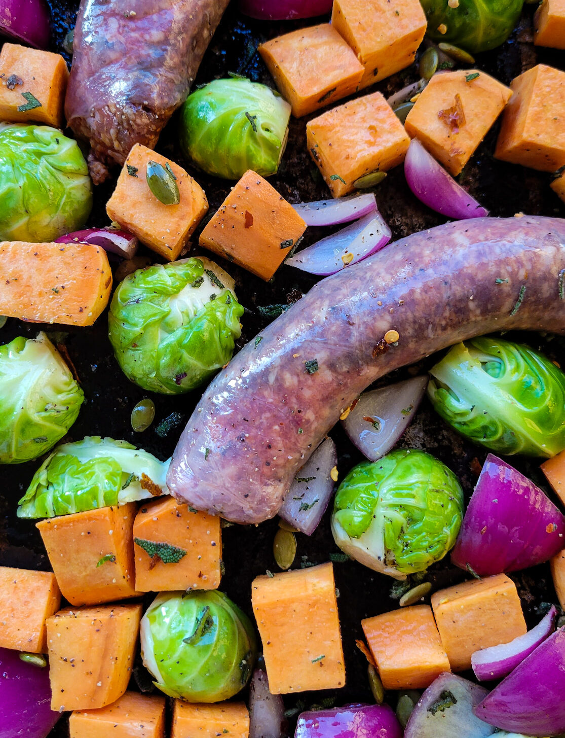 Close up of vegetables and sausages about to go into the oven for Roasted Autumn Vegetables and Sausages.