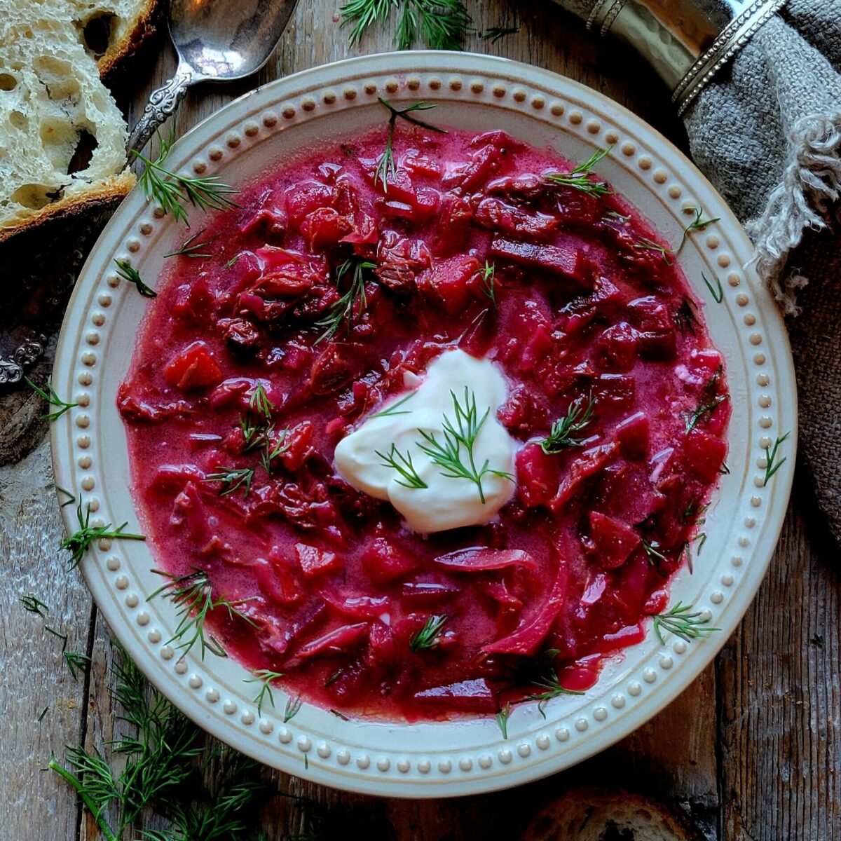 A bowl of Borscht in Short Rib Stock topped with creme fraiche and surrounded by crusty bread.