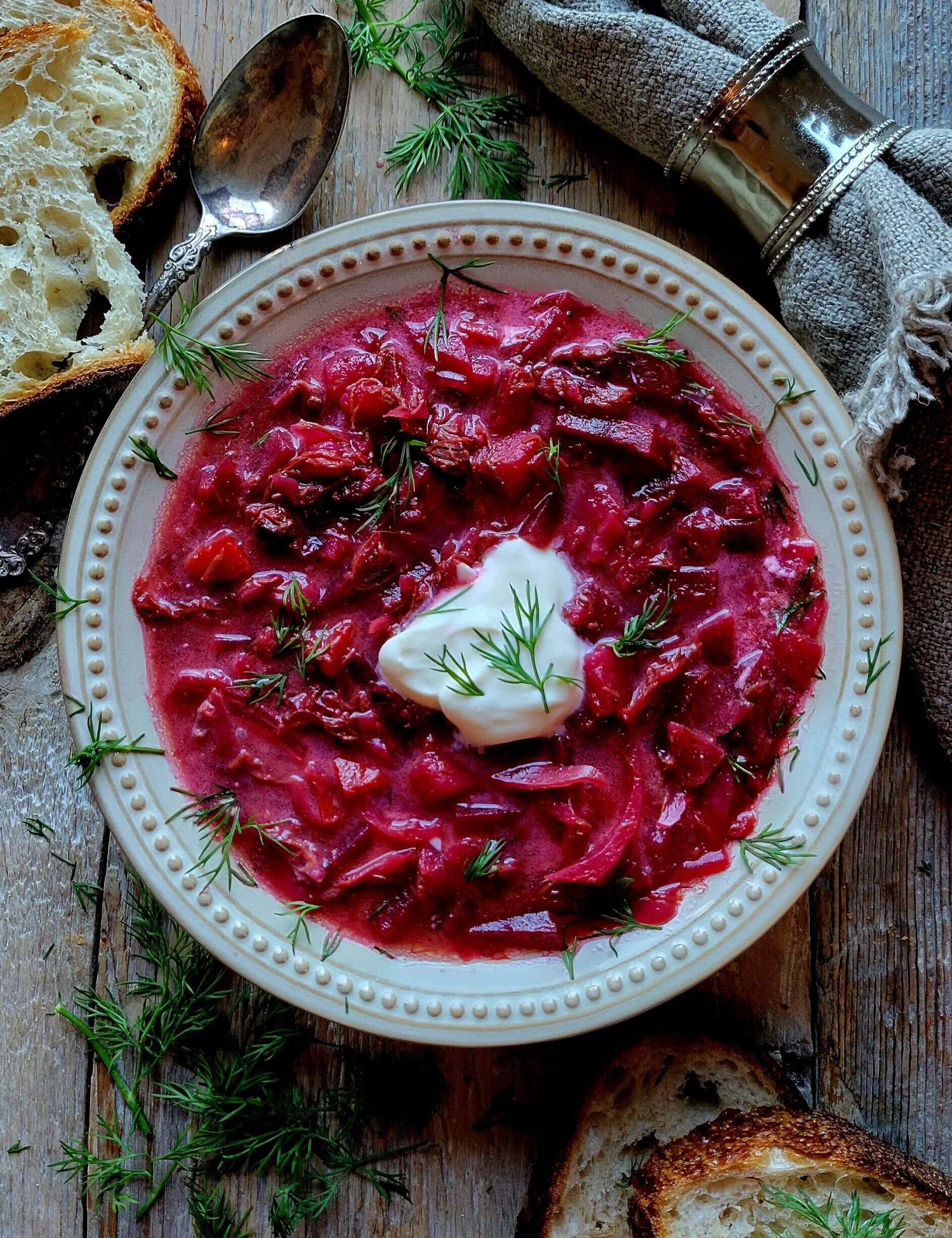 A bowl of Borscht in Short Rib Stock topped with creme fraiche and surrounded by crusty bread.