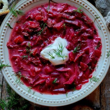 Close up of a bowl of Borscht in Short Rib Stock topped with sour cream and fresh dill.