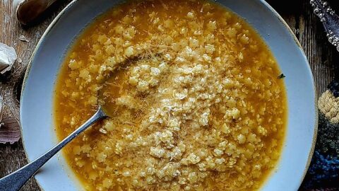 A cozy bowl of Pastina on the table with grated cheese, lemon and garlic surrounding it.