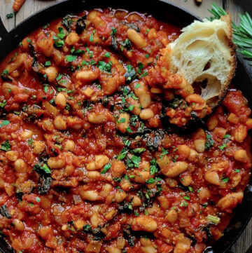A skillet filled with Tuscan Braised Beans and Kale, with a slice of crusty bread to the side.
