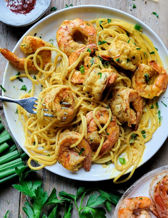 A plate of Harissa Shrimp Pasta with Saffron Sauce, with parsley scattered around the plate.