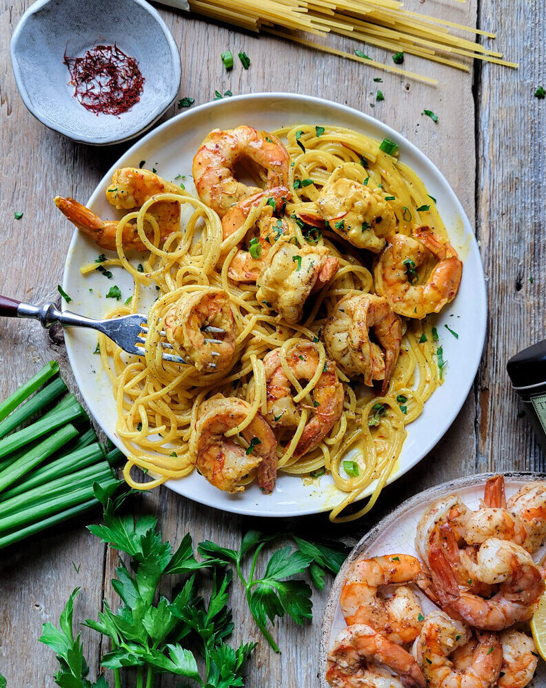 A plate with Harissa Shrimp Pasta with Saffron Sauce, with parsley and dry pasta to the side.