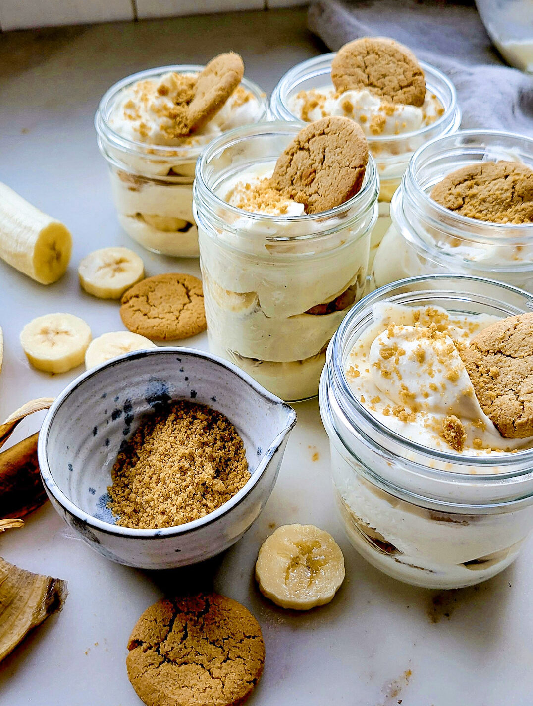 Assembling Classic Banana Pudding in mason jars, with crushed ginger snap cookies in a bowl.