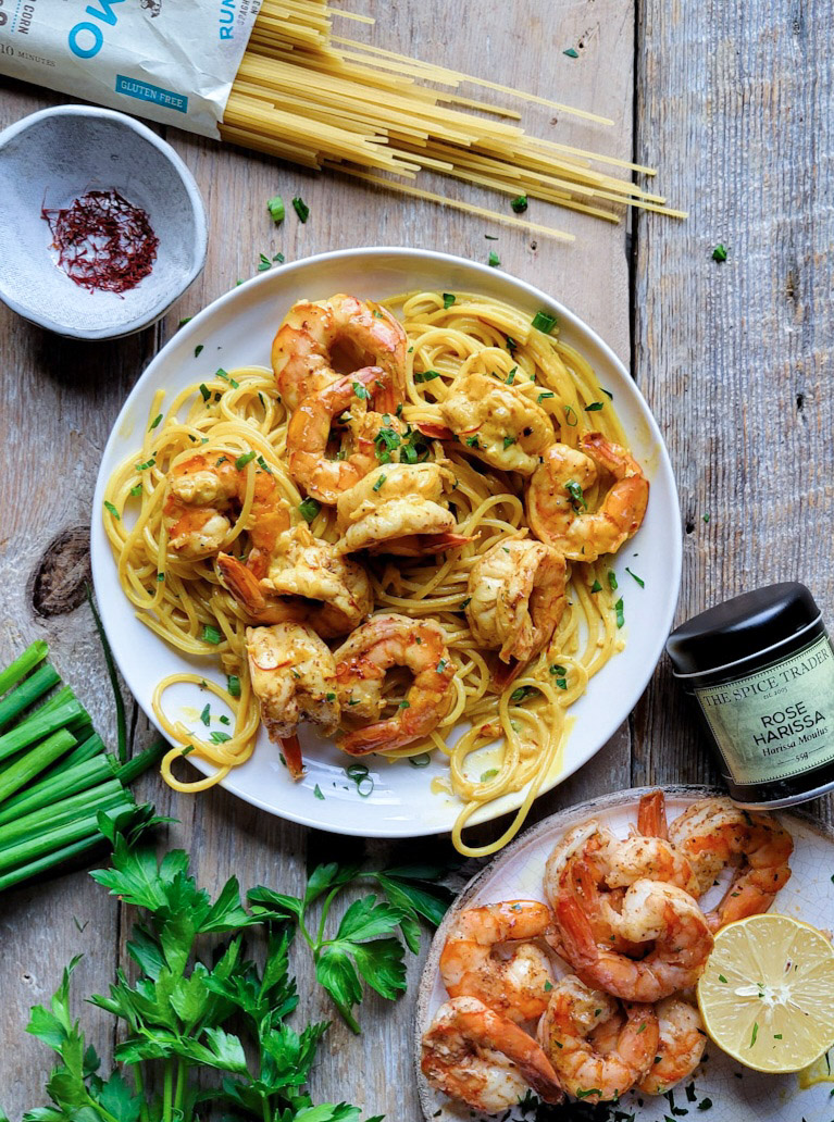 A plate filled with Harissa Shrimp Pasta with saffron sauce, with more shrimp and parsley to the side.
