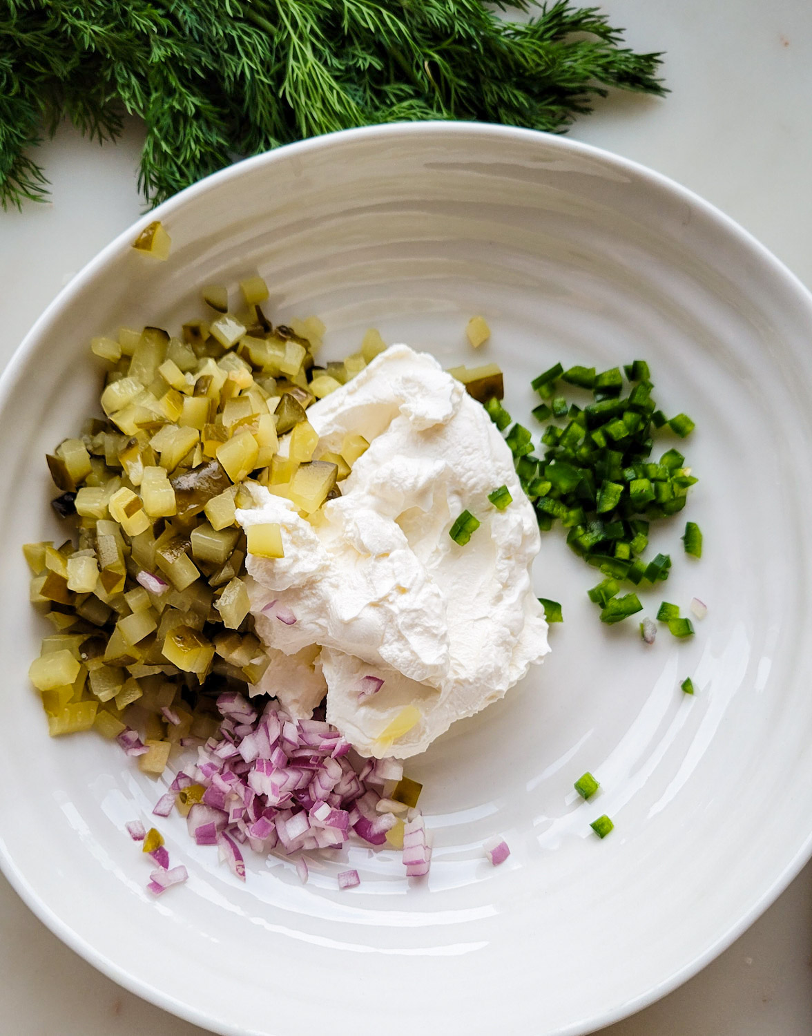 A bowl filled with the ingredients needed to make Dill Pickle Dip with Jalapeno Pepper.