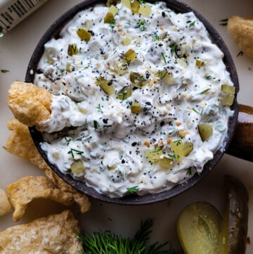 A bowl of Dill Pickle Dip with Jalapeno Pepper with some chips to the side.