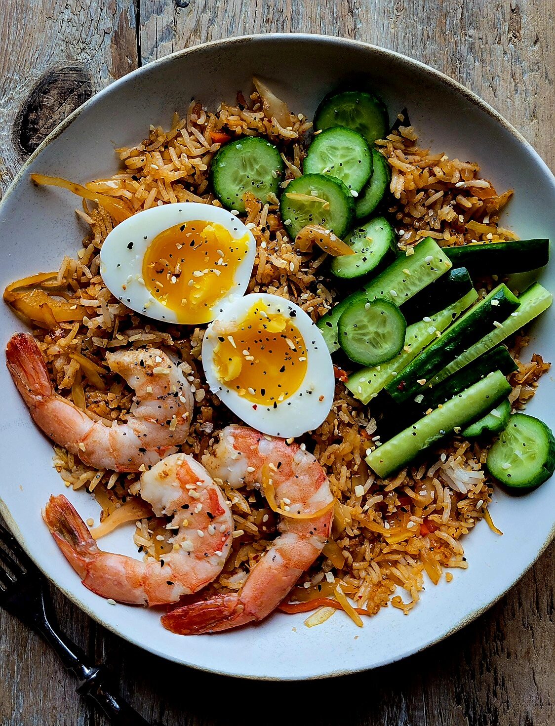A bowl of Kimchi Fried Rice topped with cucumber, jammy egg, and shrimp.