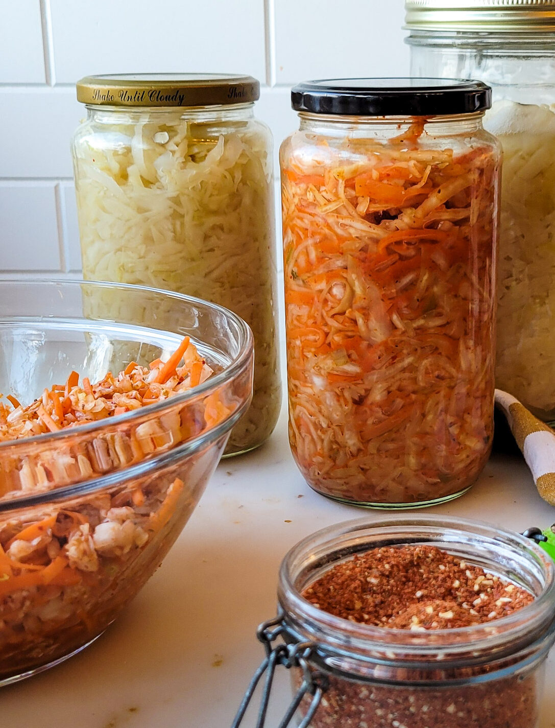 Jars of Sauerkraut and Kimchi on the counter, along with the kimchi spice blend in a jar beside them.