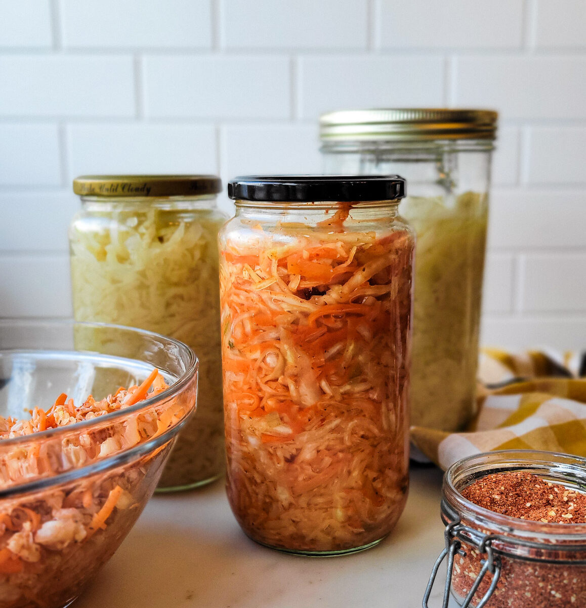 Jars of Sauerkraut and Kimchi on the counter, along with the kimchi spice blend in a jar beside them.