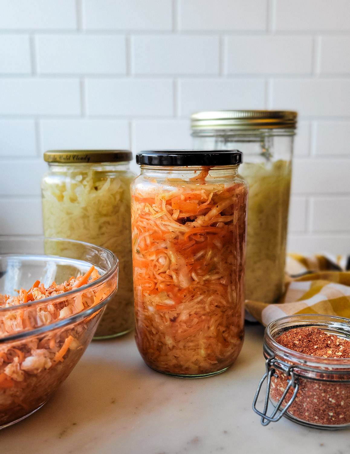 Jars of Sauerkraut and Kimchi on the counter, along with the kimchi spice blend in a jar beside them.