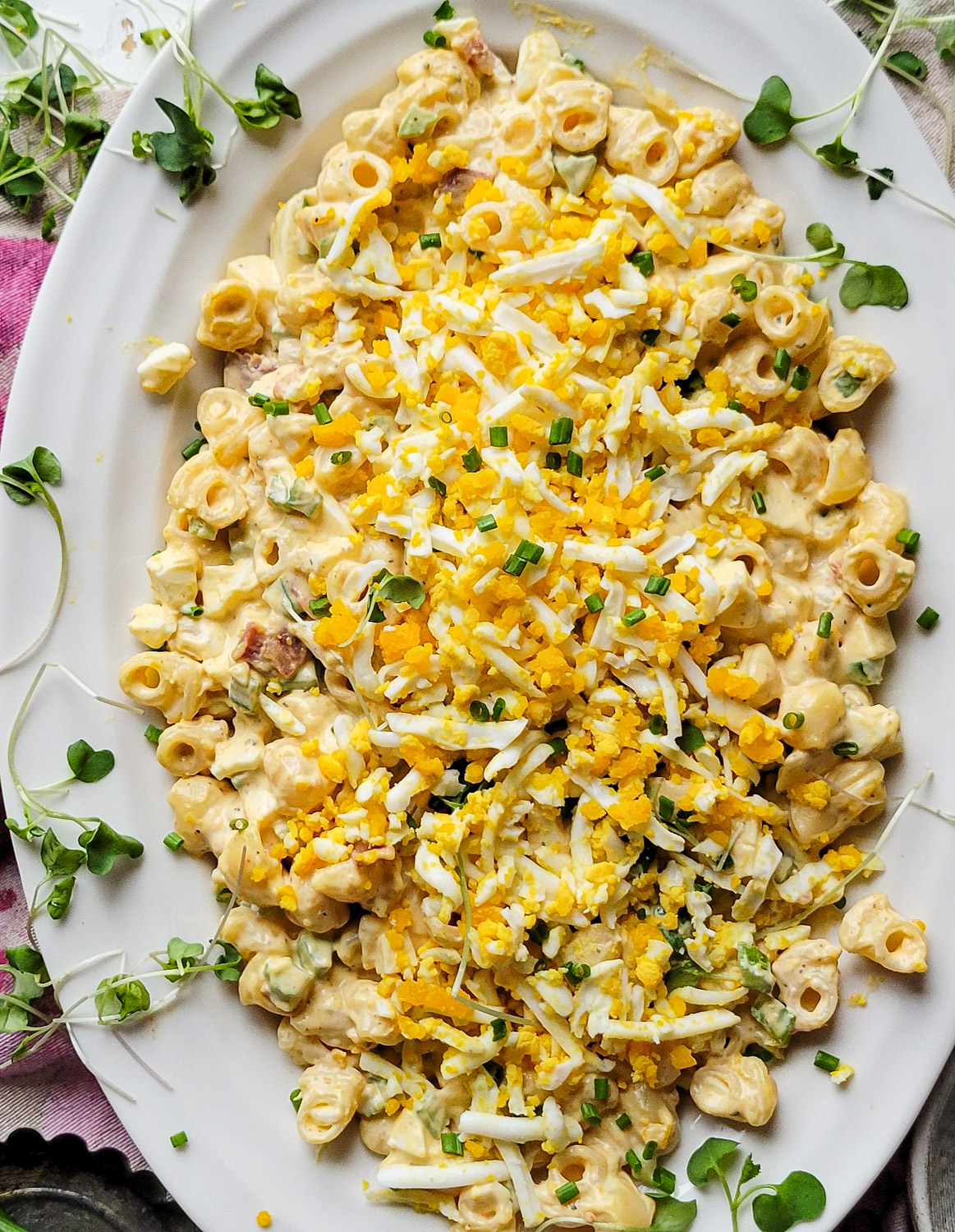 A platter filled with Mimosa Egg Pasta Salad with spring green shoots scattered about.