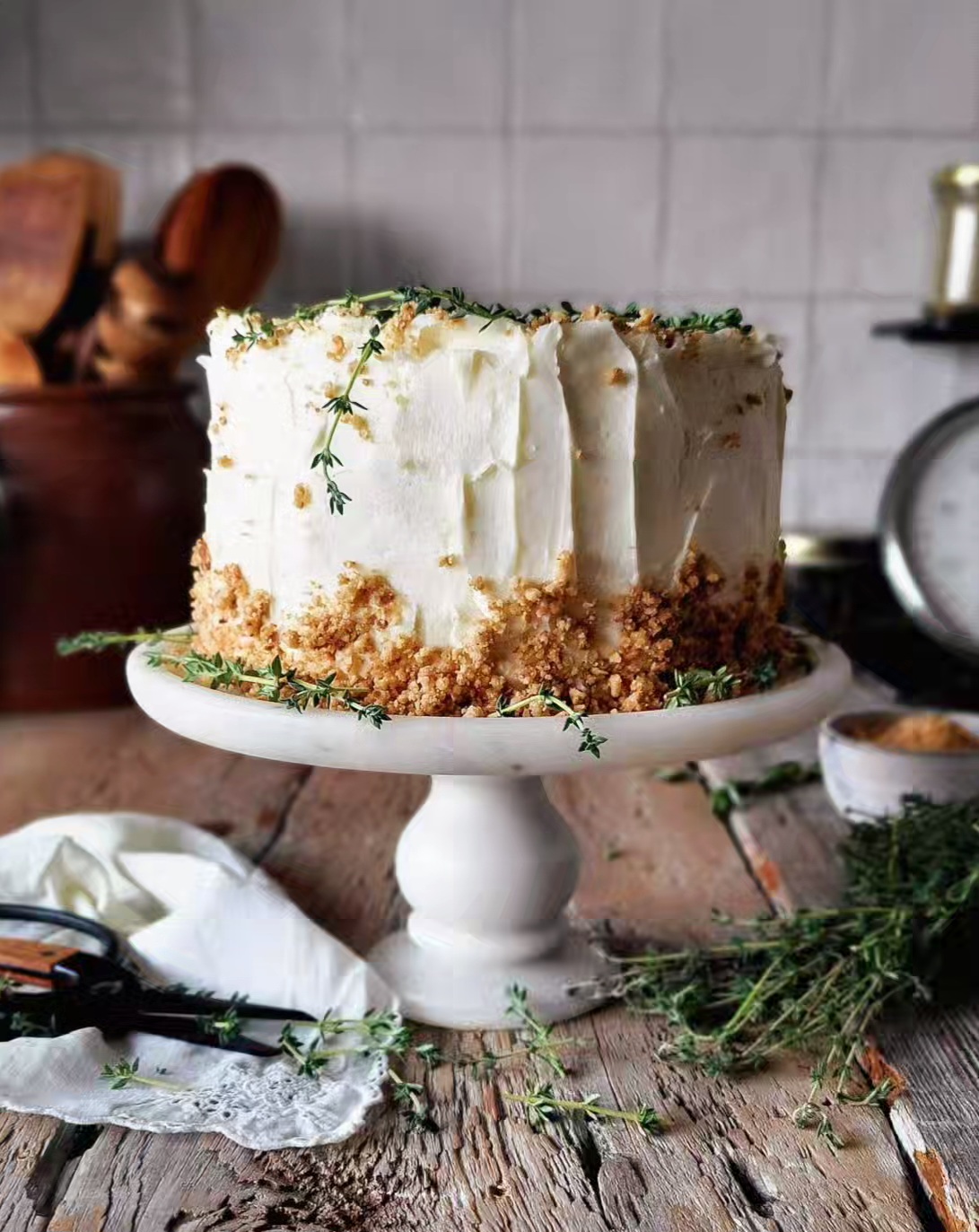 The Best Carrot Cake with Ginger Cream Cheese Frosting sits on stand with fresh thyme sprigs to the side.