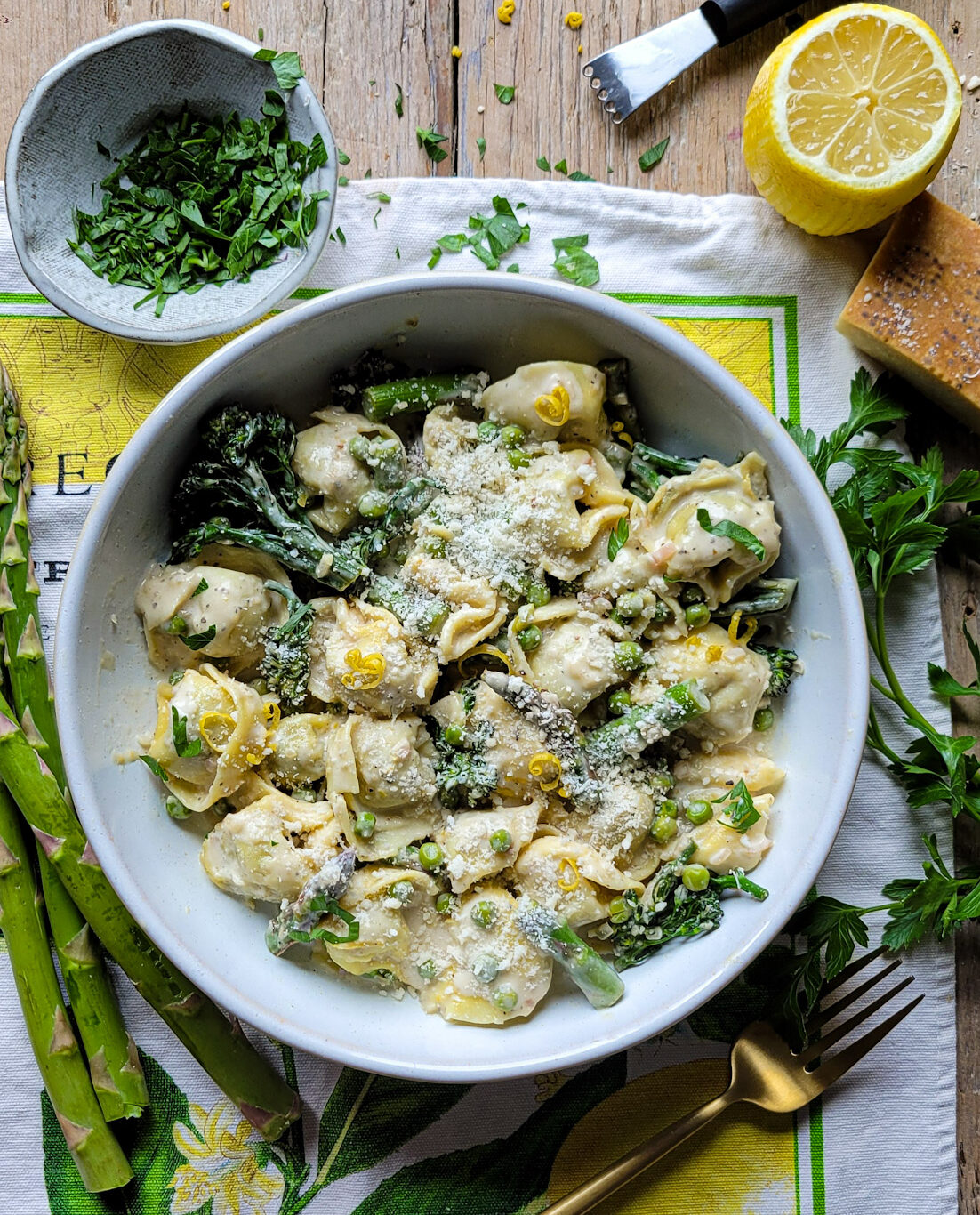 A bowl filled with Lemon Cream Pasta and Spring Vegetables surrounded by chopped parsley and lemon slices