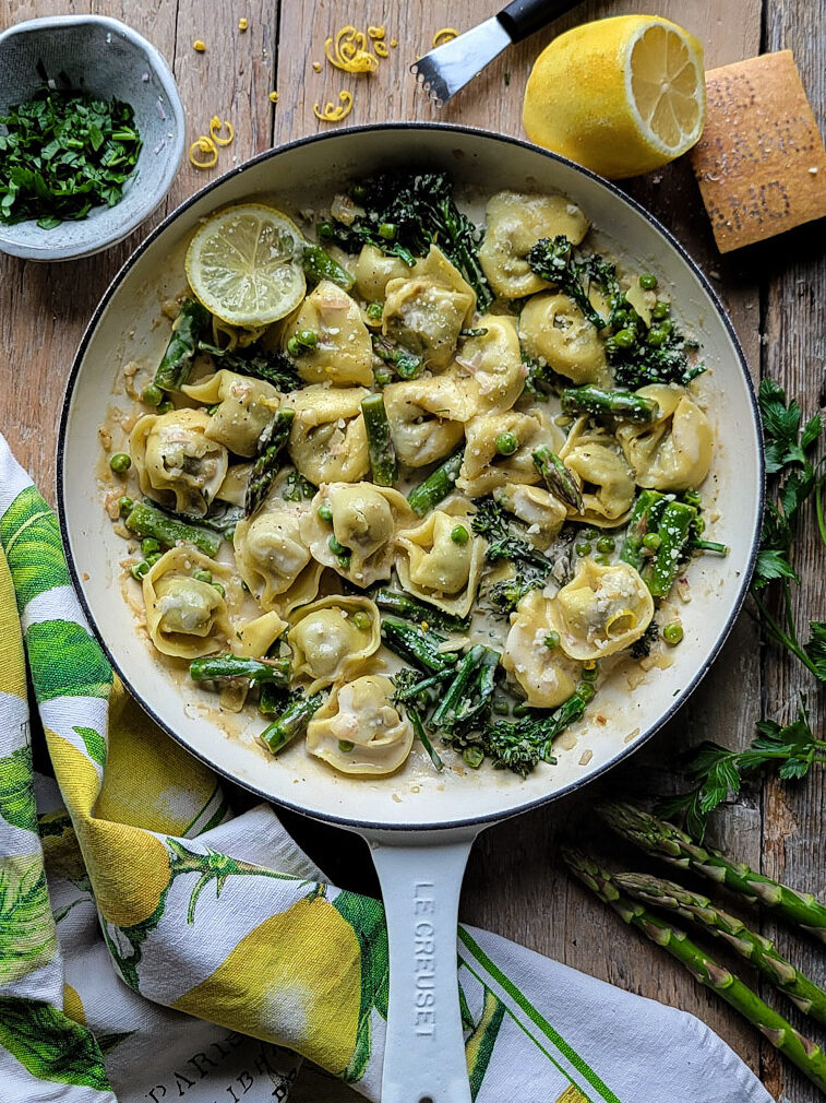 Lemon Cream Pasta with Spring Vegetables in a skillet surrounded by fresh asparagus, lemon zest and chopped parsley