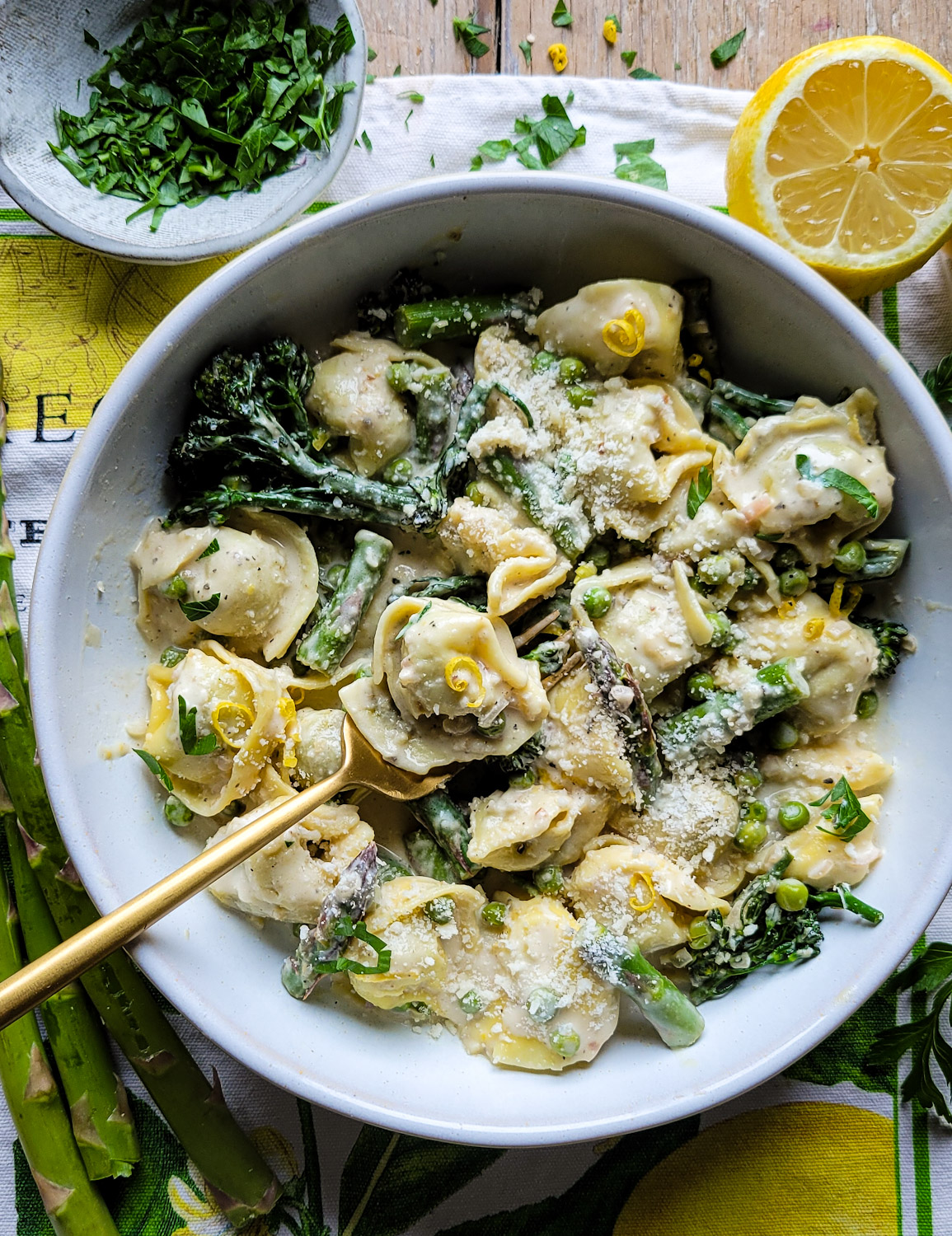 A bowl of Lemon Cream Pasta with Spring Vegetables with a fork holding some pasta is on the table, with fresh asparagus and parsley in the background.