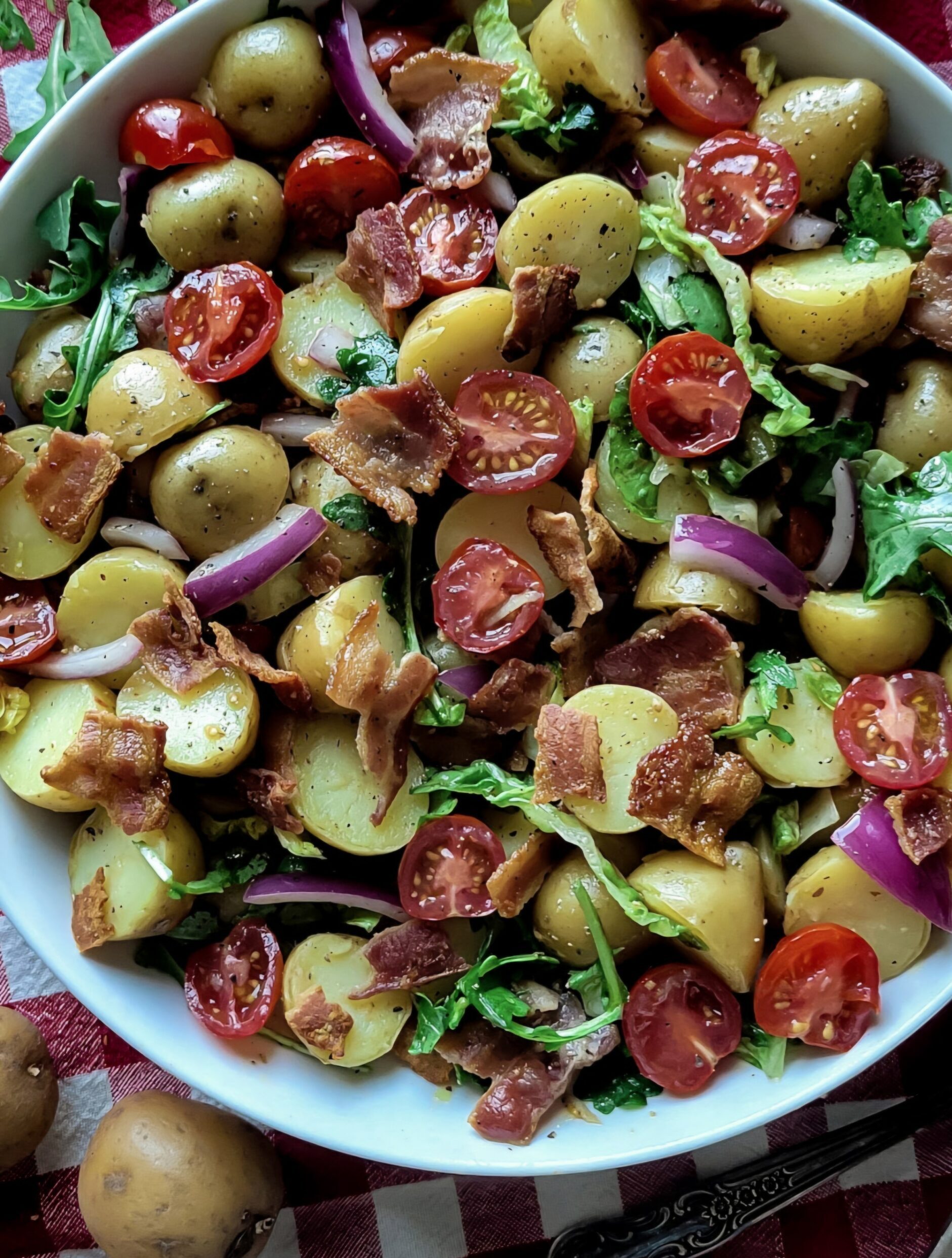 Close up of a succulent BLT Potato Salad, with mini potatoes, bacon, arugula, grape tomatoes, and red onion.
