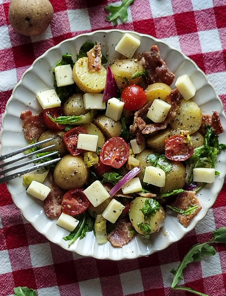A plate of BLT Potato Salad sits on a red checkered picnic cloth.