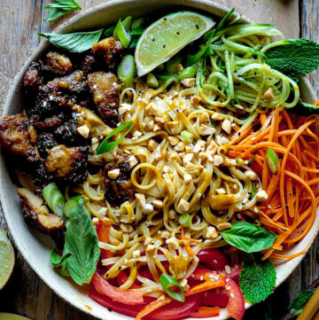 A Bowl filled with Chicken Satay, Peanut Noodles, and vegetables to create a flavour packed Satay Noodle Bowl in on the table, with mint leaves and limes to the side.