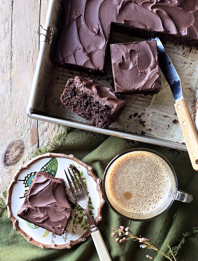 Sliced Chocolate Zucchini Cake with one slice on a plate and a coffee to the side.