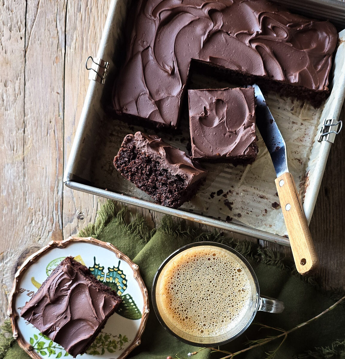 Sliced up Double Chocolate Zucchini Cake with one slice on a plate and a coffee to the side.