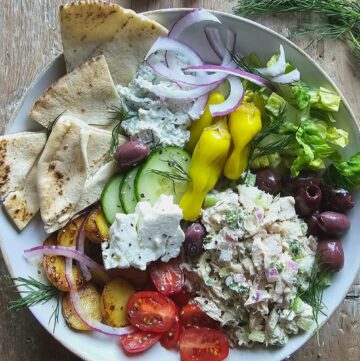 A bowl filled with Tzatziki Chicken Salad, and all the Greek sides, with pita slices to the side.