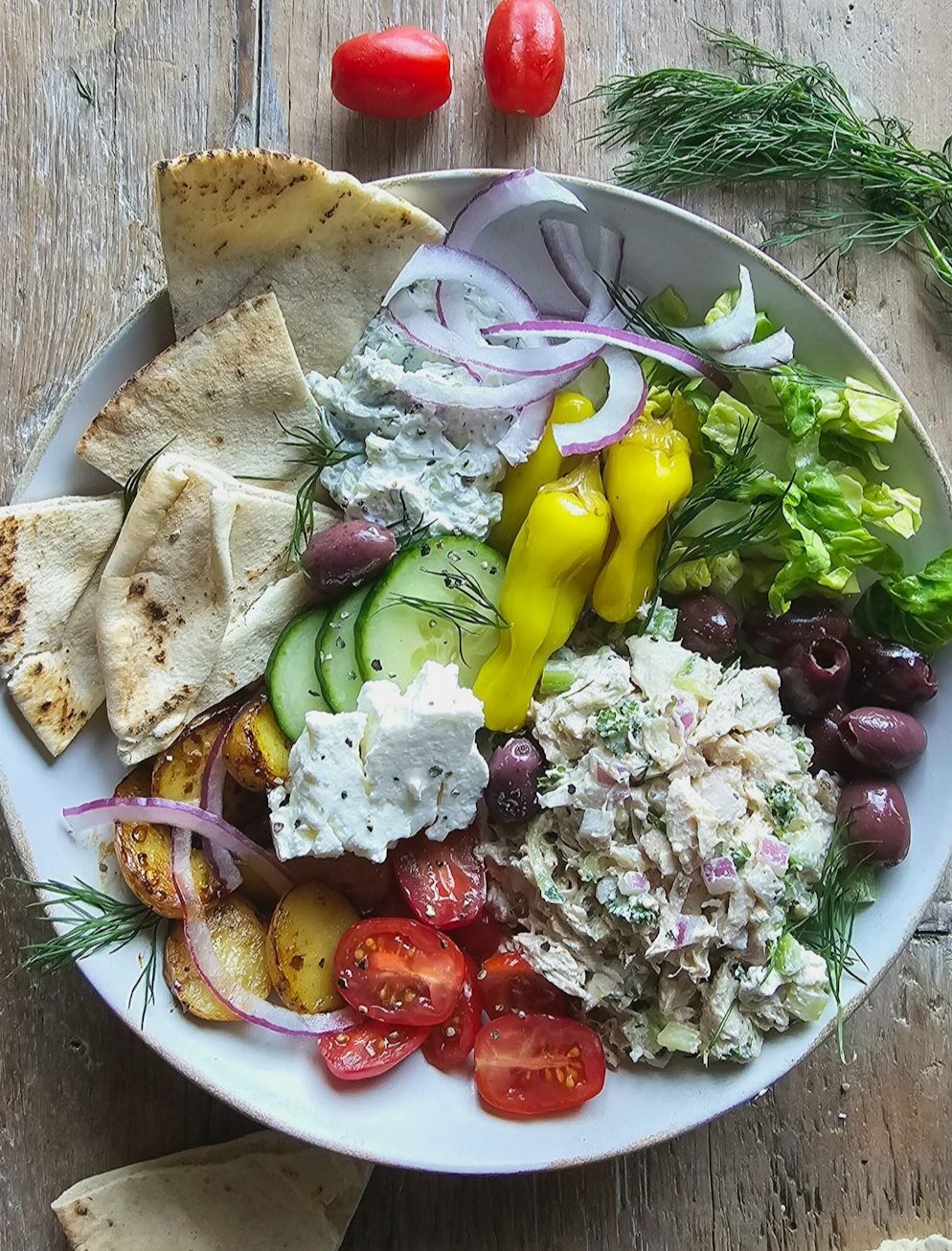 A bowl filled with Tzatziki Chicken Salad, and all the Greek sides, with pita slices to the side.