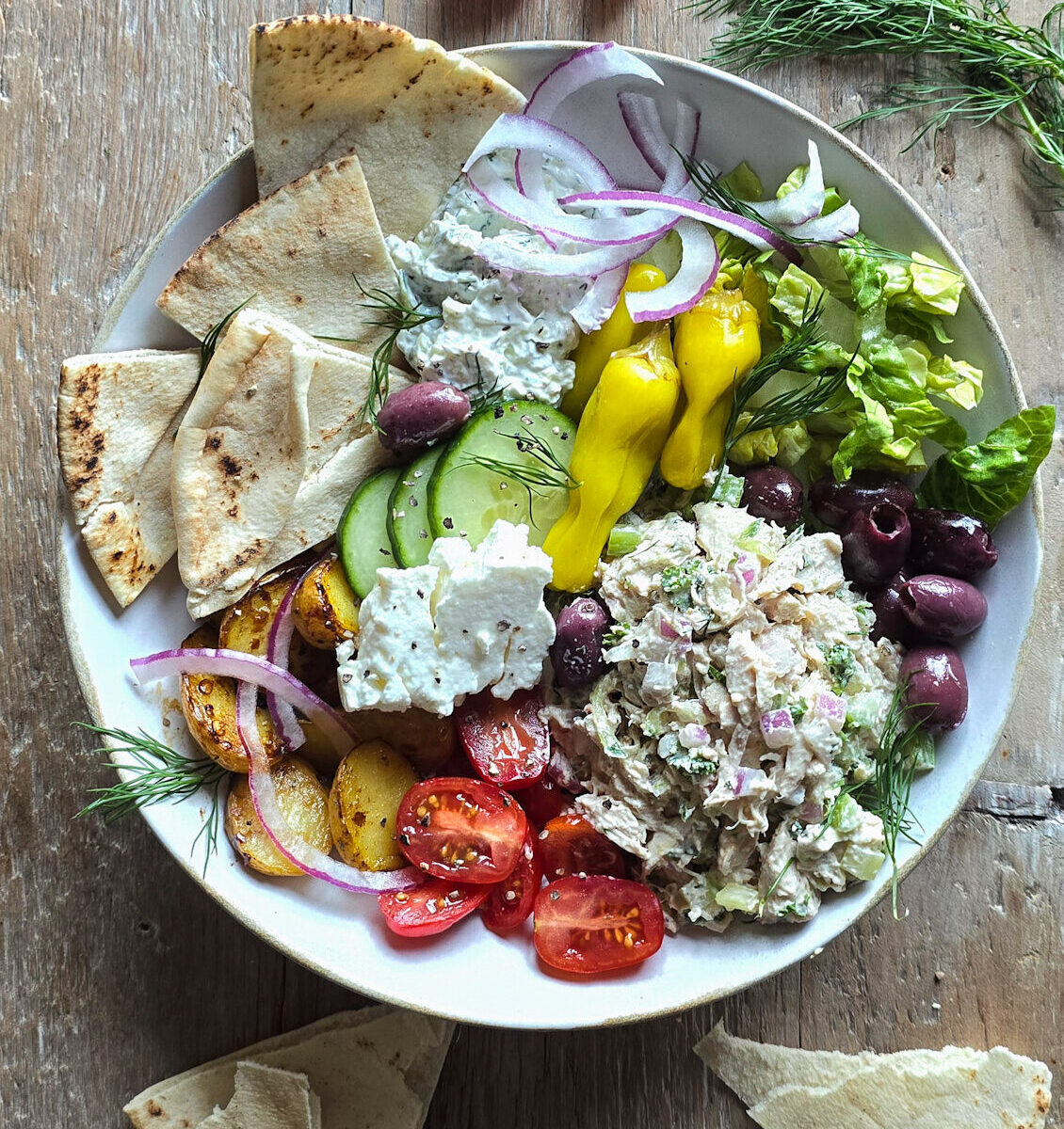 A bowl filled with Tzatziki Chicken Salad, and all the Greek sides, with pita slices to the side.