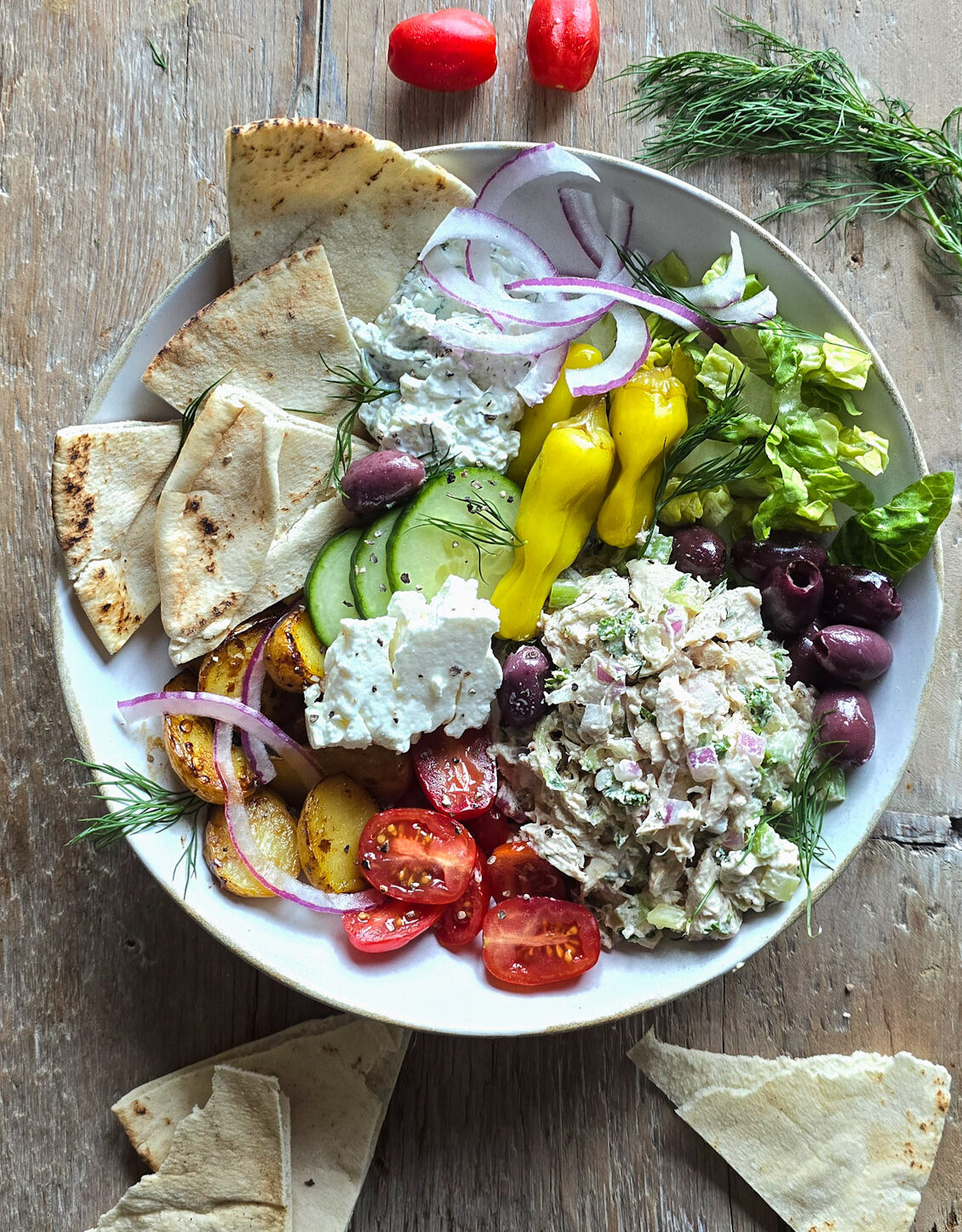 A bowl filled with Tzatziki Chicken Salad, and all the Greek sides, with pita slices to the side.