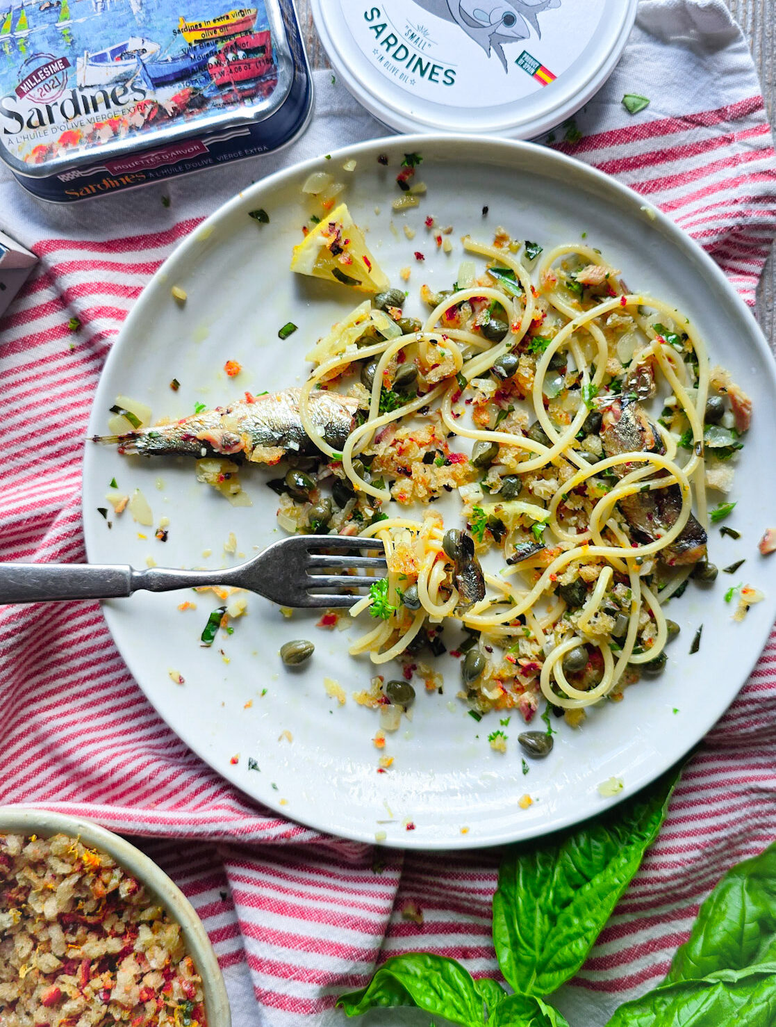 A plate with mostly eaten Sardine and Lemon Pangrattato Pasta on the table, with tins of fish to the side.