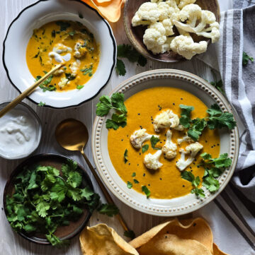 Two bowls of Curry Cauliflower Soup are on the table, with crispy pappadums on the side to eat with the soup.