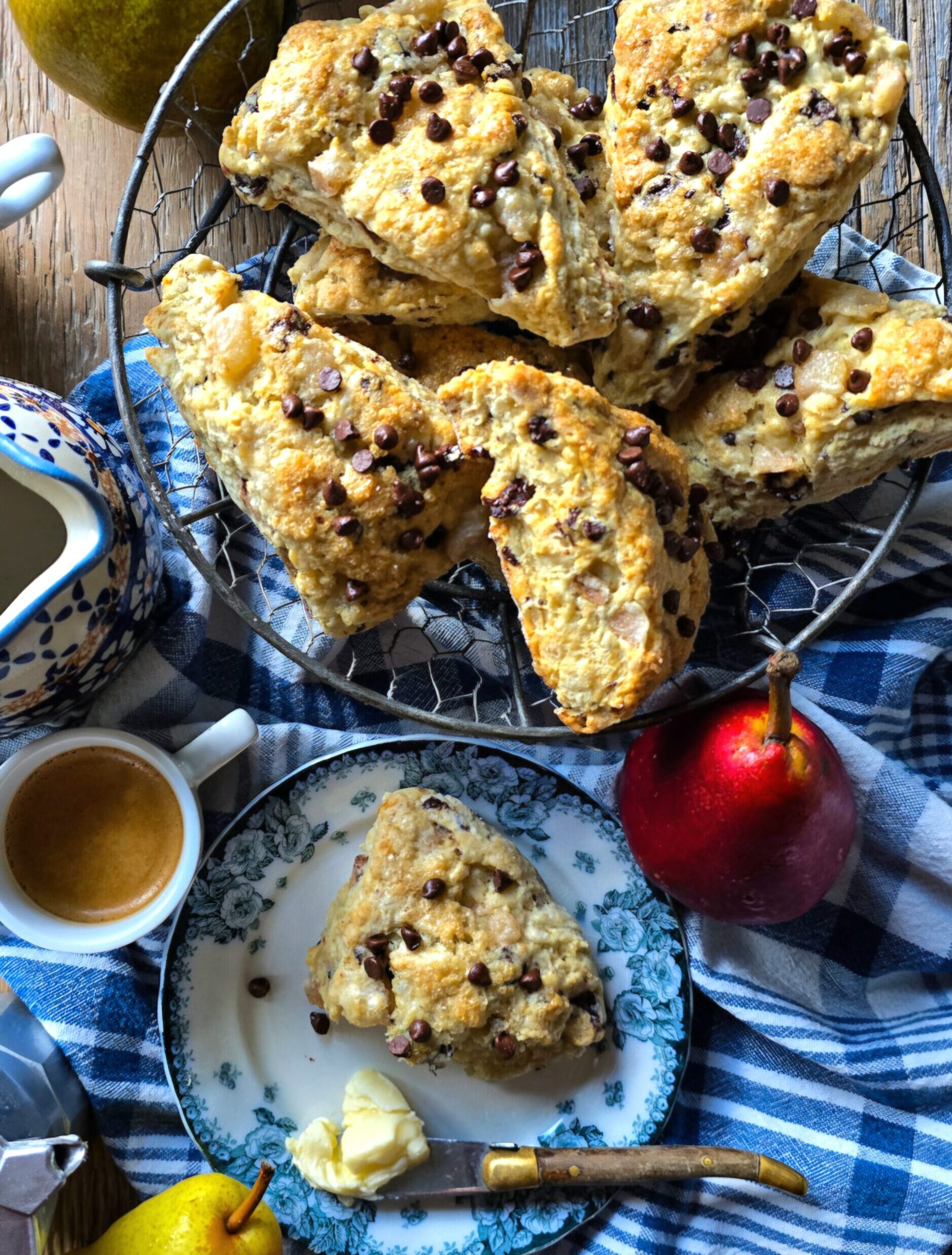 A basket of freshly baked Pear Chocolate Scones is on the table along with a fresh pears and coffee cups.