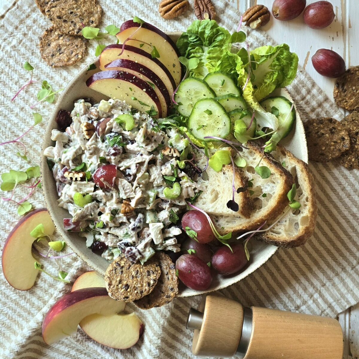 A bowl filled with Leftover Diner Turkey Salad, crackers, grapes, sliced apples and nuts sits on the table, surrounded by crackers and more apple slices.