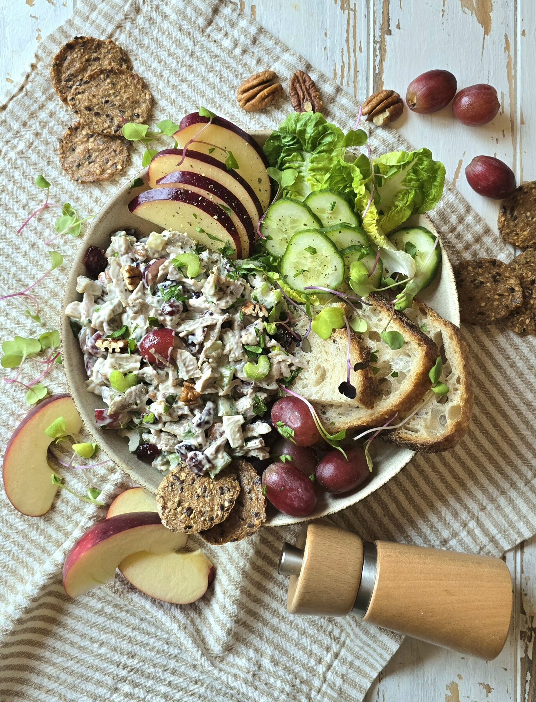 A bowl filled with Leftover Diner Turkey Salad, crackers, grapes, sliced apples and nuts sits on the table, surrounded by crackers and more apple slices.