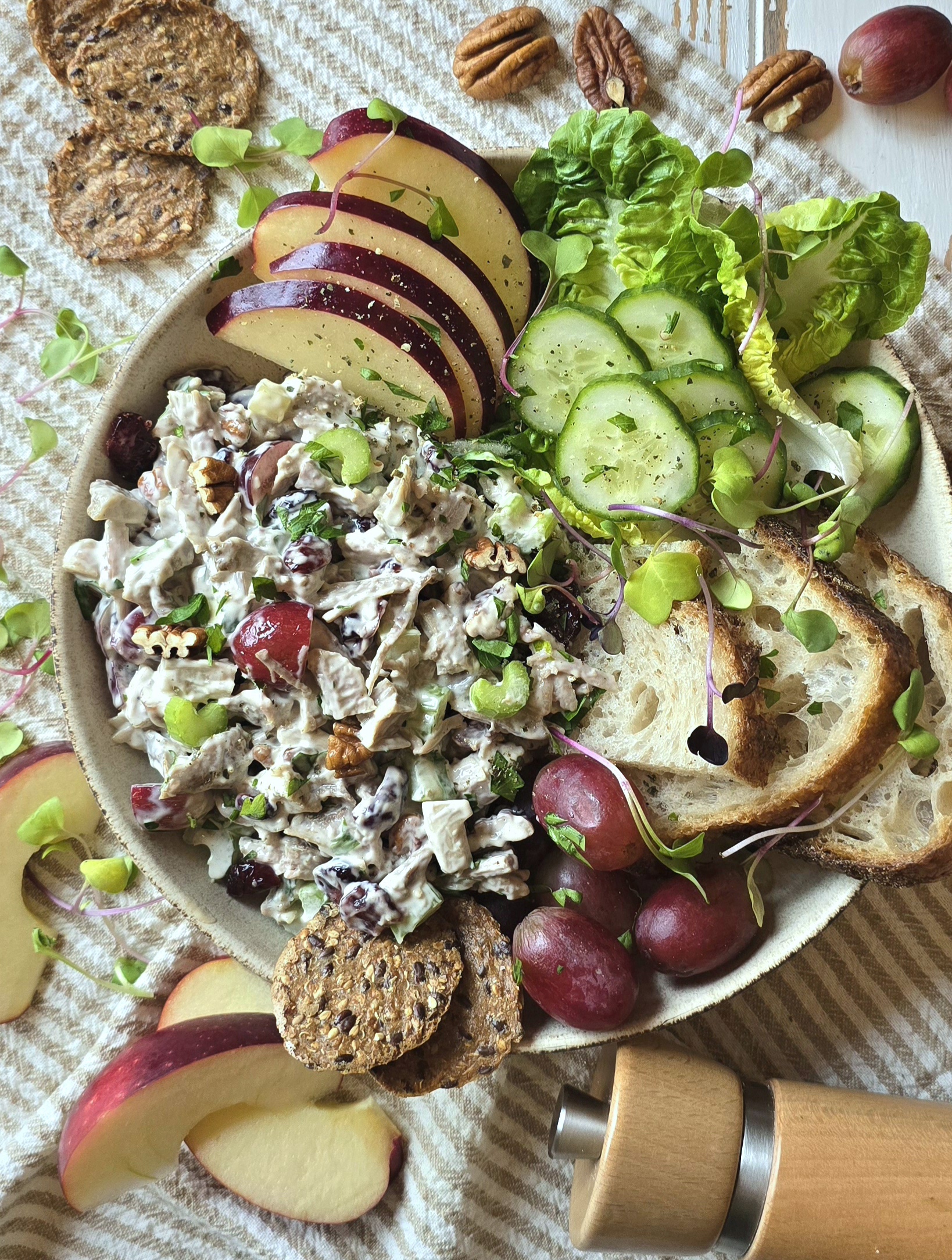 Close up of a Bowl filled with Leftover Diner Turkey Salad, with crackers, cucumbers, apple slices and grapes sitting on a table.