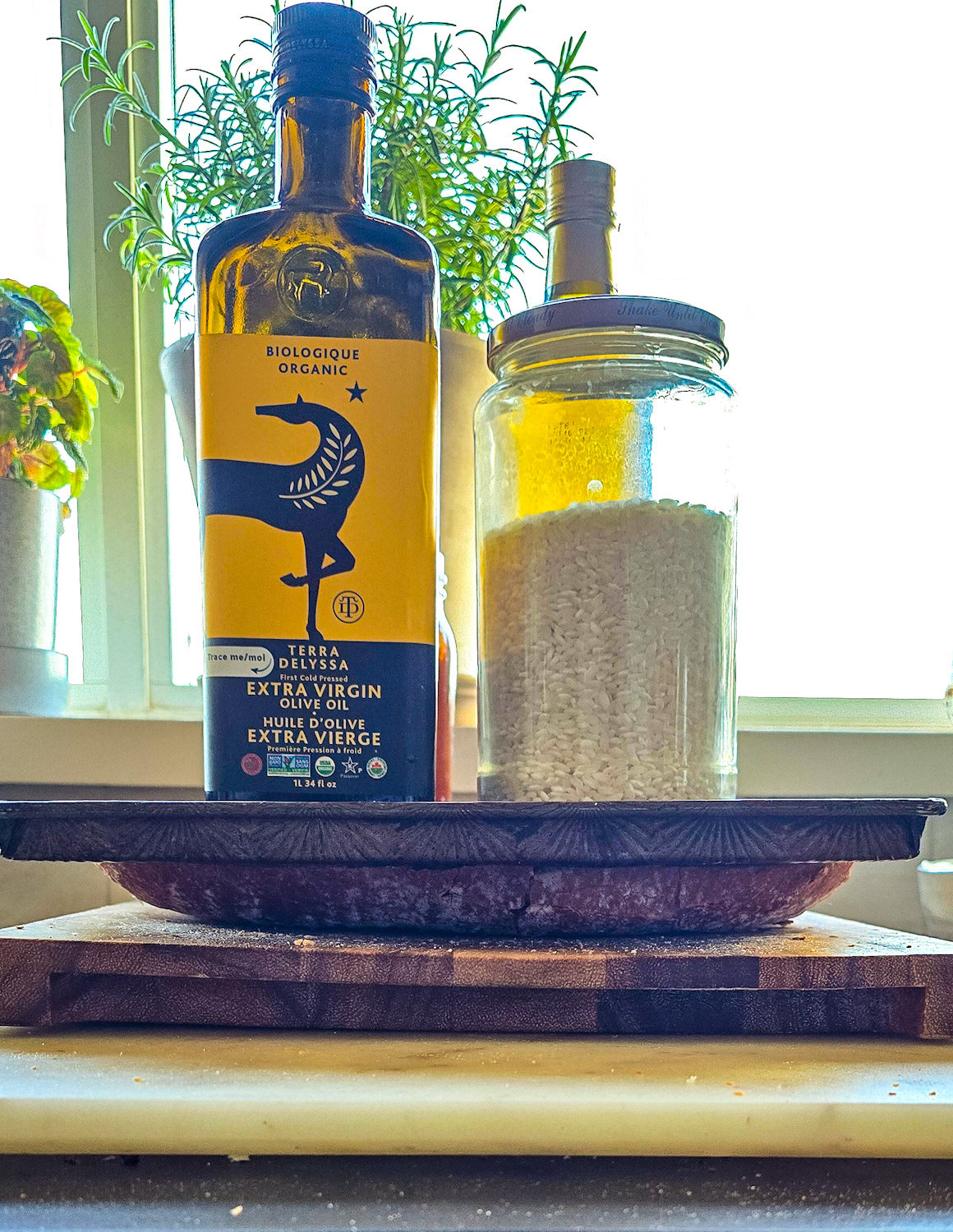 Method of preparing french bread for turning it into pizza. The halves of bread are being pressed down by placing a baking sheet on top of the halves, weighed down with bottles of olive oil and heavy jars.