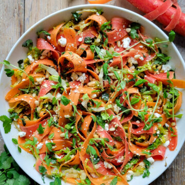 A finished Carrot Ribbon Salad is in a bowl topped with pea sprouts and feta cheese.