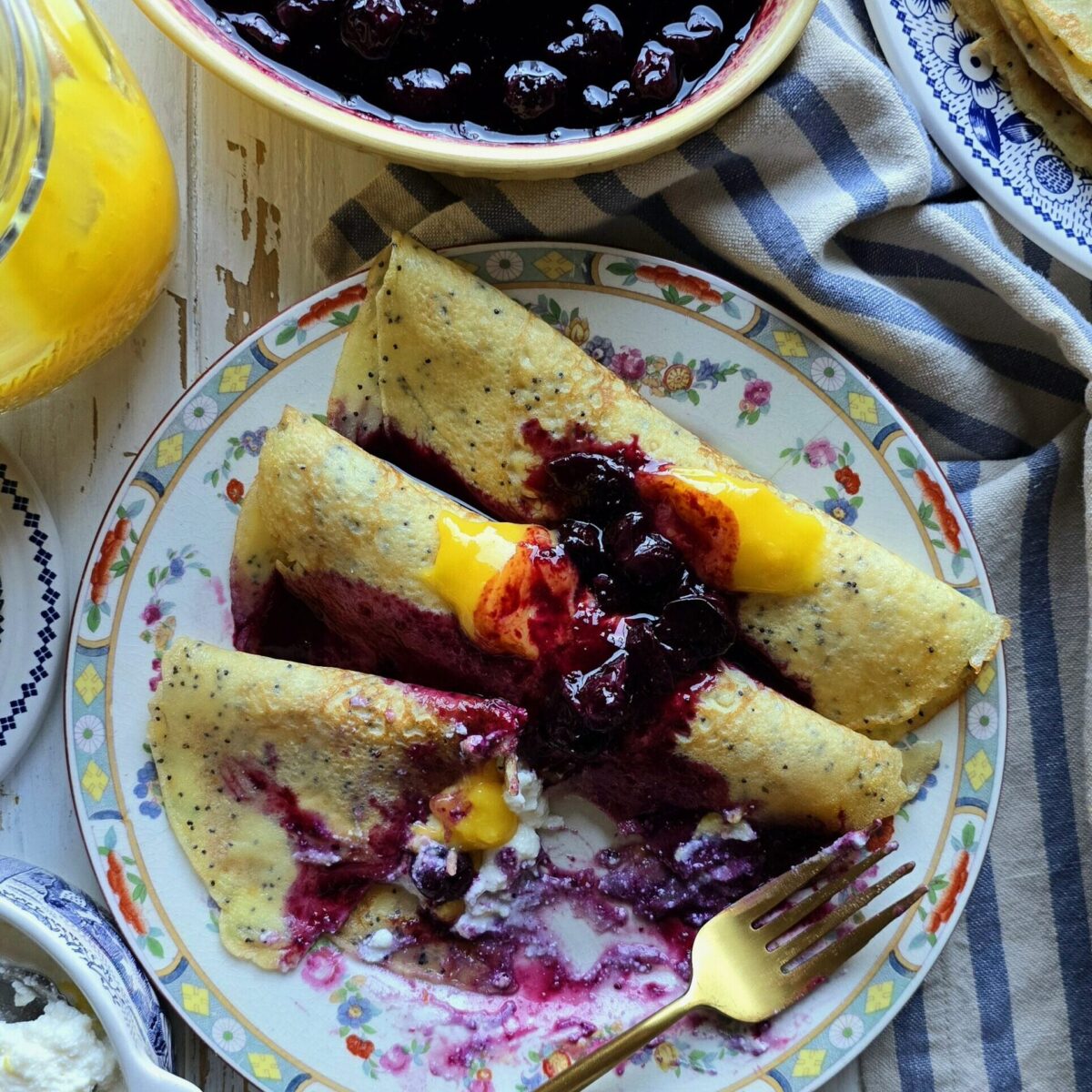Partially eaten Lemon Poppyseed Crepes with blueberry sauce on a plate sitting on the table.