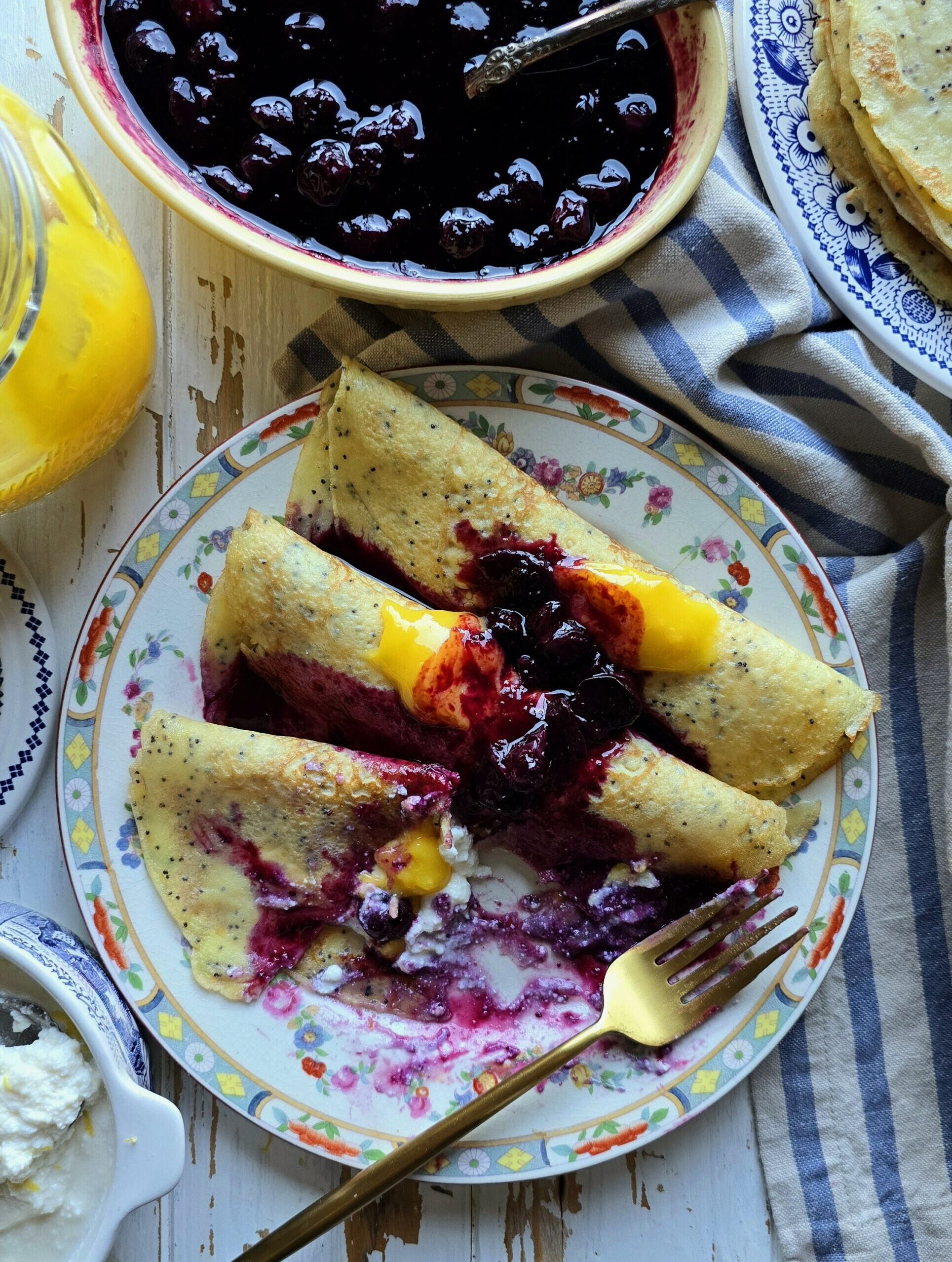 Partially eaten Lemon Poppyseed Crepes with blueberry sauce on a plate sitting on the table.