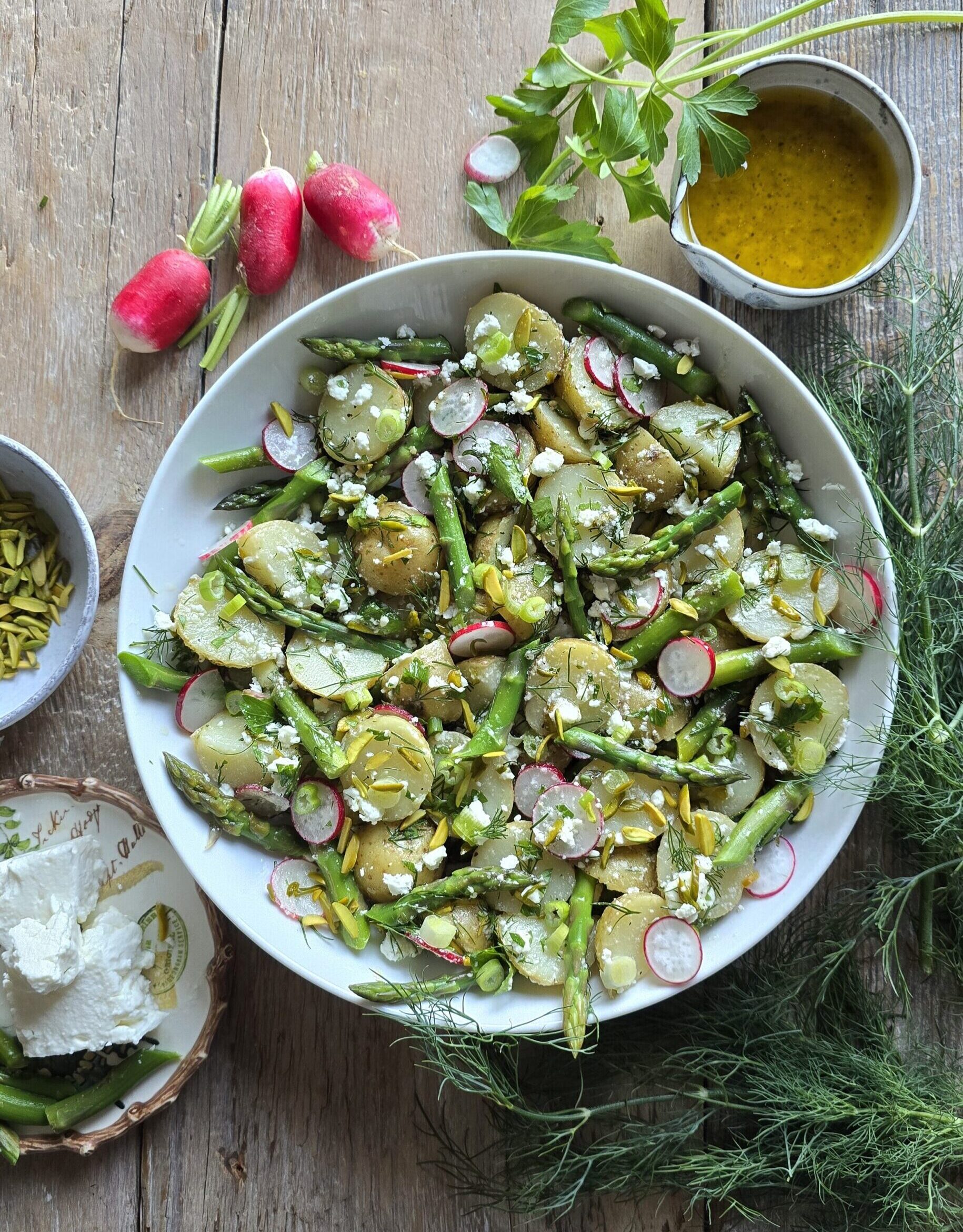 A bowl filled with Potato Asparagus Salad is on the table, with Lemon Honey Vinaigrette and radishes to the side.