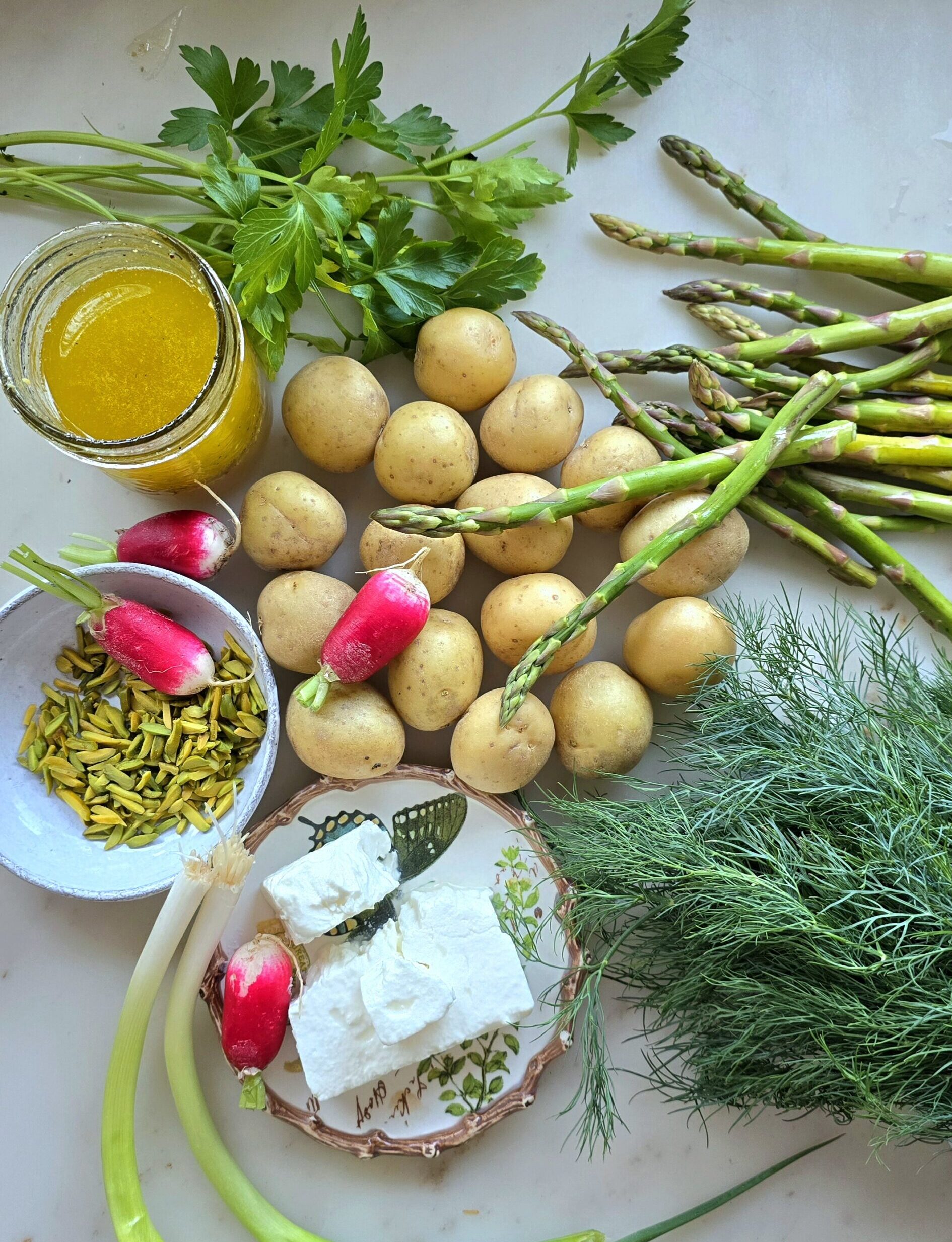 Ingredients needed to make a Potato Asparagus Salad with Lemon Honey Vinaigrette are spread out on the counter.