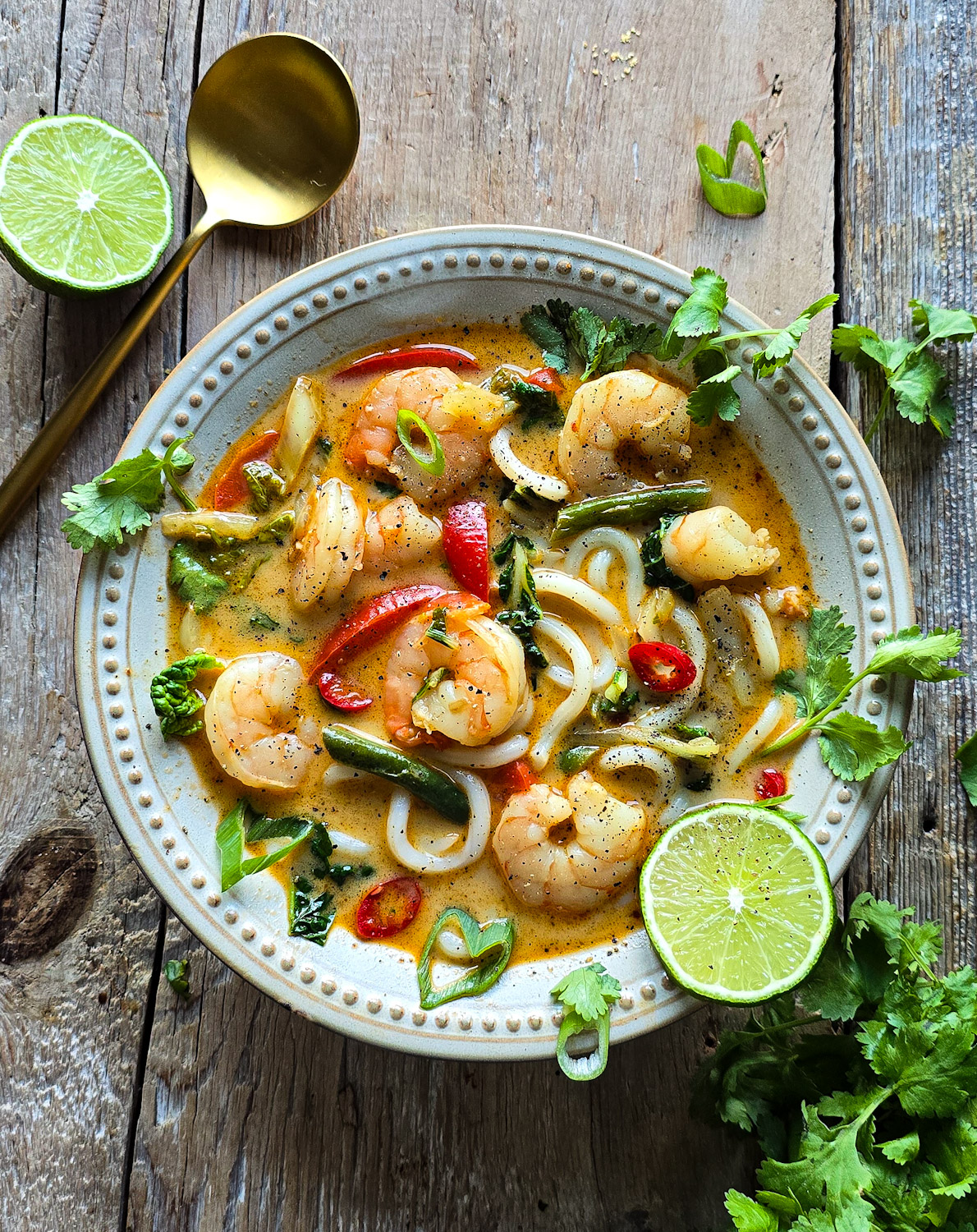 A bowl of Thai Fish Curry Soup sits on the table, with lime slices to the side, as well as fresh cilantro.